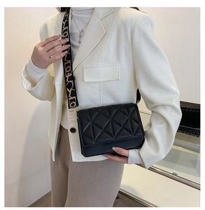 Detail of black quilted shoulder bag featuring artistic wide strap with geometric patterns