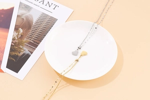 Elegant gold and silver heart-shaped stainless steel necklaces displayed on a white plate