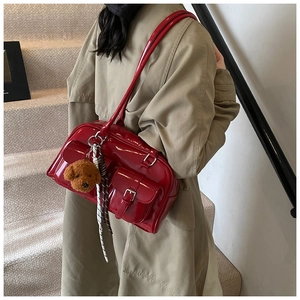 Close-up of a glossy red patent leather shoulder bag with bear pendant and front pockets