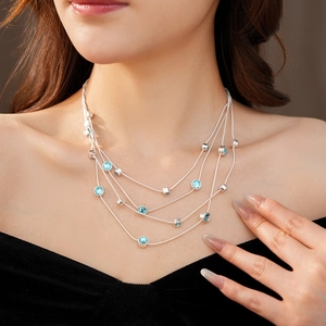 Close-up of layered silver necklace with sparkling blue zircon gems on a female model