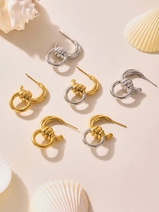 Flache Ansicht gedrehter C-förmiger Ohrringe in Gold und Silber auf Muschelhintergrund