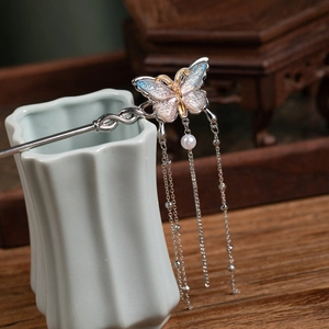Detail of a butterfly hair stick with blue enamel, long tassels and a white pearl accent
