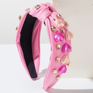 Diadema rosa con nudo y cristales de corazón sobre soporte de piedra blanca