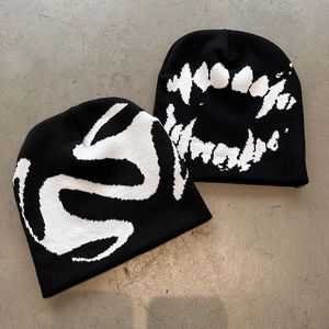 Street style black knit beanie with white fang pattern on a textured gray background