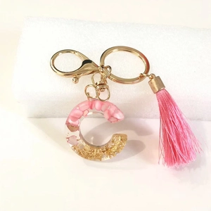 Close-up of pink resin letter C keychain with gold foil flakes and a soft silk tassel