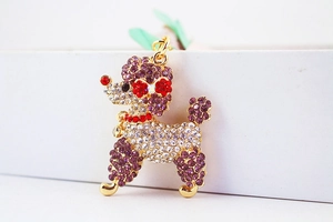 Nahaufnahme des goldenen Pudel-Schlüsselanhängers mit lila Kristallen auf Geschenkbox