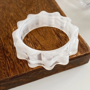 Macro detail of wave-edged resin bangle with white marble texture on wooden base