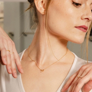Dettaglio del set collana con fiocco dorato con orecchini e anelli indossati dal modello