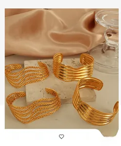 Detail of four gold geometric wave cuff bracelets on marble with silk background