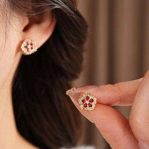 Detail of flower stud earrings with red petals and gold base held by hand