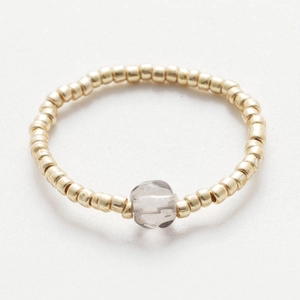 Macro shot of handmade beaded ring with gold round beads and a clear raw crystal stone