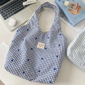 Detailaufnahme der blau-weiß karierten Canvas-Tasche mit Blumenstickerei und gewebtem Etikett