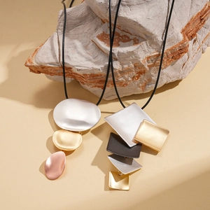 Minimalist geometric matte metal pendant necklaces with long black cords on natural stone