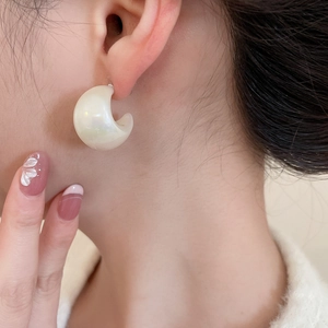 Close-up of elegant creamy white acrylic C-shaped earrings with a pearlescent finish on model