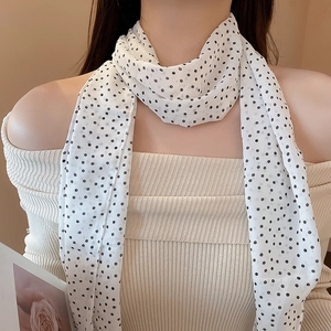 Detailed close-up of a white polka dot scarf tied on neck with beige ribbed knit top