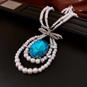 Macro detail of triple-layer pearl necklace with blue oval gemstone and crystal bow