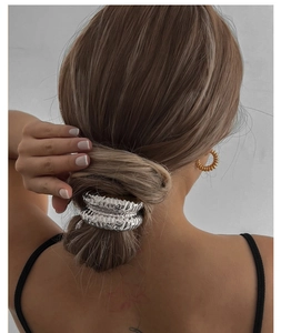 Close-up of textured silver metal cuff hair tie securing a low bun on a female model