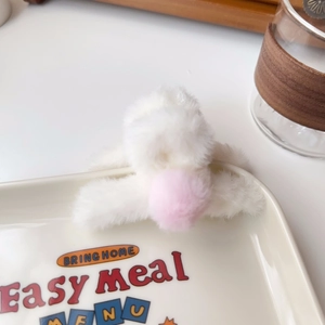 Detail shot of a small white plush hair claw clip featuring a soft pink pom-pom decoration