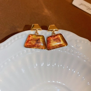 Close-up of geometric earrings with gold metal and amber resin texture on a white plate