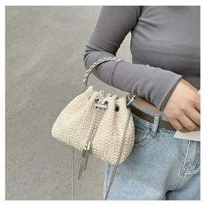 Detail of beige straw bucket bag with metal ring handle and chain drawstring on model