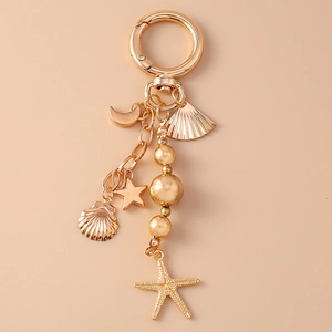 Llavero dorado con colgantes de luna, concha y estrella de mar sobre fondo rosado