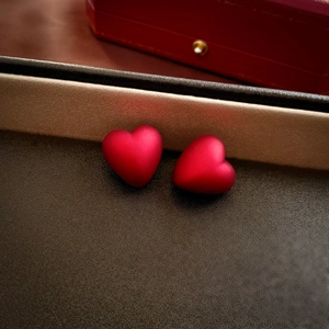Macro detail of red velvet matte heart-shaped stud earrings on a leather texture background