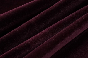 Detailansicht von dunkelweinrotem Samtstoff mit elegantem Faltenwurf und sanftem Glanz