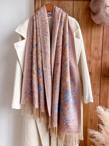 Detail of ethnic pattern scarf with tassels on beige coat and wooden hanger