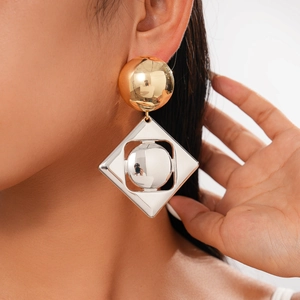 Close-up of geometric gold ball and silver hollow rhombus pendant earrings on a model