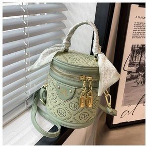 Close-up of green cylinder bucket bag with letter embossing and silk scarf handle