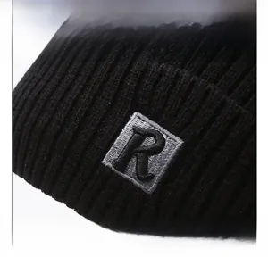 Close-up of black ribbed knit beanie featuring a grey square patch with embroidered R letter