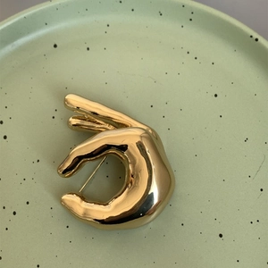 Macro d'une broche geste OK dorée avec finition métallique polie sur plat céramique