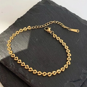 Detailed close-up of 18k gold plated heart chain bracelet with lobster clasp on dark stone