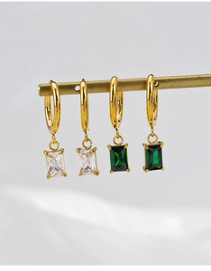 Detailed close-up of hanging gold earrings with white and emerald green square zircons