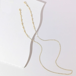 Gold-plated cross link eyeglass chain over geometric white props with soft lighting