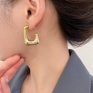 Close-up of polished gold U-shaped geometric drop earrings worn with a modern minimalist style