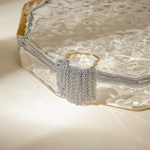 Detailed shot of two-tone gold and silver chain tassel ring on water-textured glass