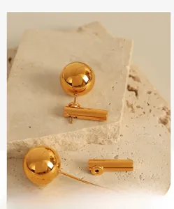 Detailed close-up of gold geometric spherical earrings on a textured travertine stone surface
