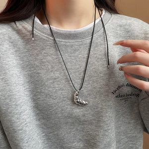 Detail showing a silver croissant pendant necklace on a black minimalist leather cord