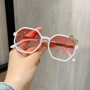 Close-up of white octagonal kids sunglasses with pink gradient lenses and golden bow detail
