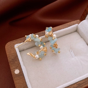 Macro detail of blue stone and pearl C-shaped earrings on a vintage wooden jewelry box