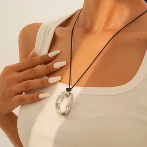 Minimalist silver polished round pendant necklace with black cord worn by a model