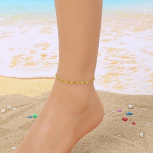 Close-up of gold chain anklet with lime green beads worn on an ankle at the beach