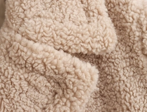 Gros plan sur le tissu polaire sherpa abricot montrant la texture bouclée et douce