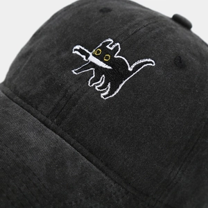 Close-up of black corduroy baseball cap featuring detailed cartoon cat embroidery