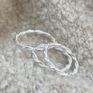 Macro detail of three S925 sterling silver twisted rope rings on white soft fabric