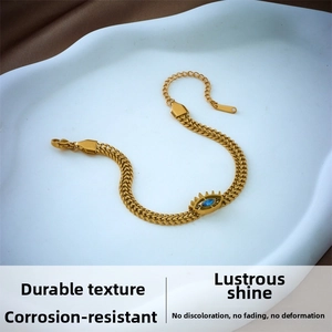 Detail of gold snake chain bracelet with evil eye charm on white ceramic tray