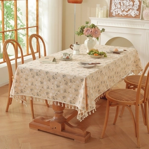 Detailed view of beige rectangle tablecloth with white floral pattern and fringe edges