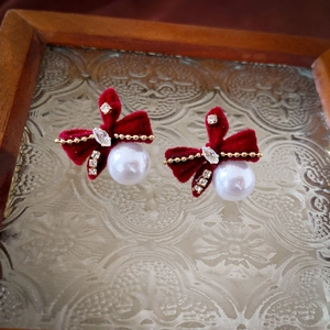 Détail de boucles d'oreilles nœud en velours rouge avec perles sur plateau en verre