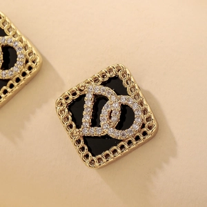 Détail de boucles d'oreilles losanges dorées avec émail noir et lettre D sertie de diamants